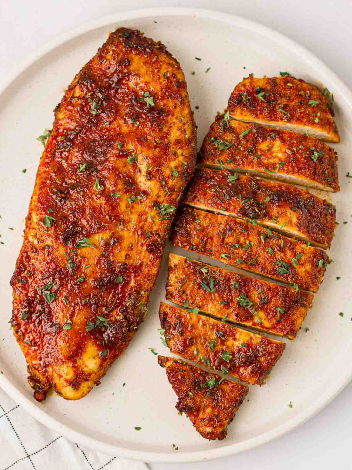 Two chicken breast slices cooked in the air fryer with a sticky, brown coating, on a white plate