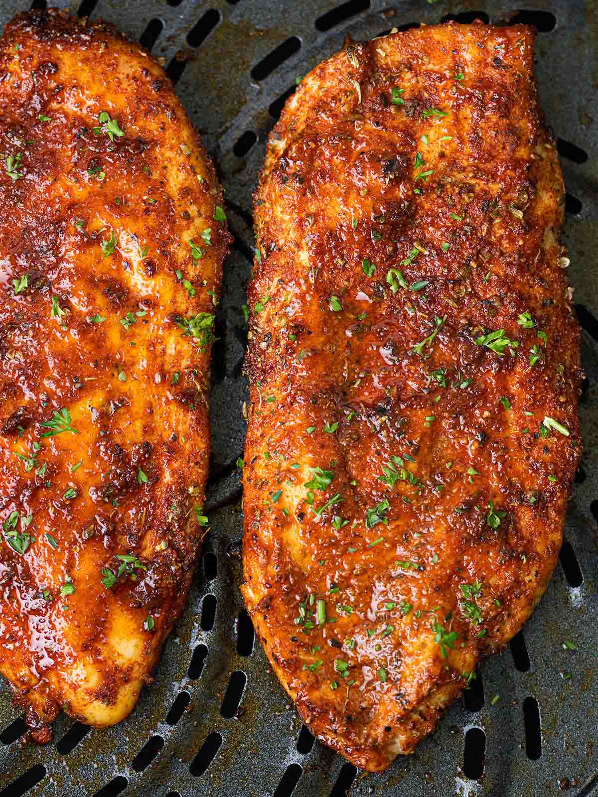 A close up of two chicken breasts cooking in an air fryer.