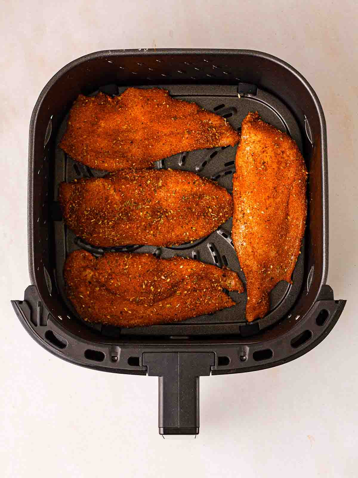 Four chicken cutlets coated and in an air fryer, ready to be cooked.