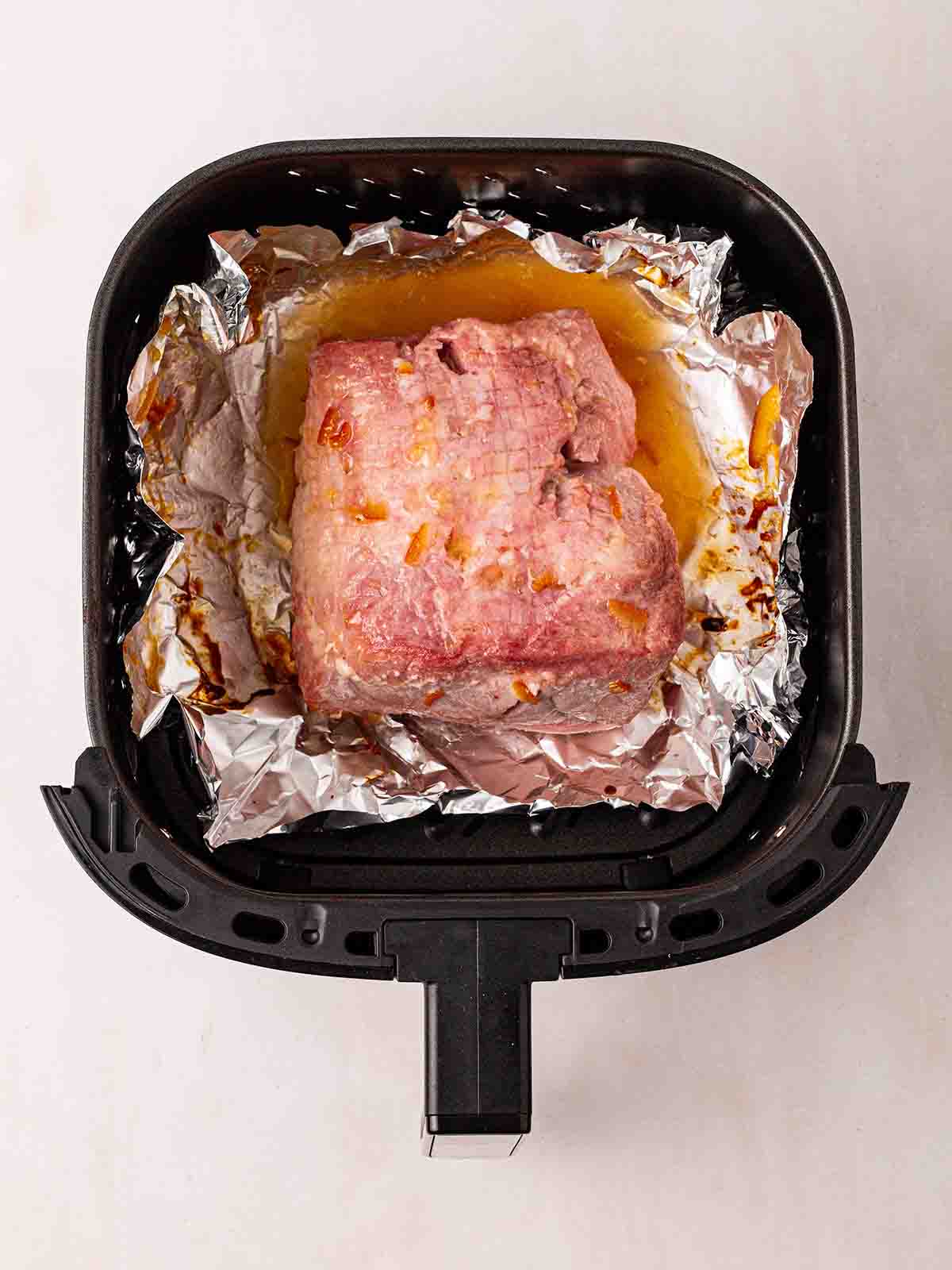A half cooked gammon joint in an air fryer with foil underneath and an orange honey glaze.