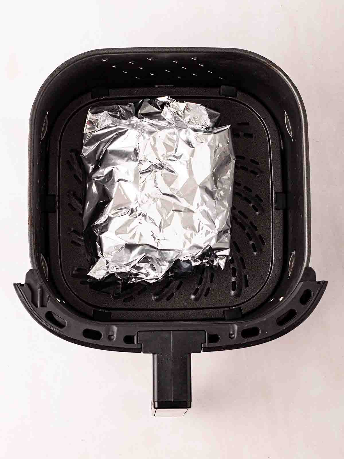 An air fryer tray with a foil parcel, for step 4 in the method for Air Fryer Gammon recipe.