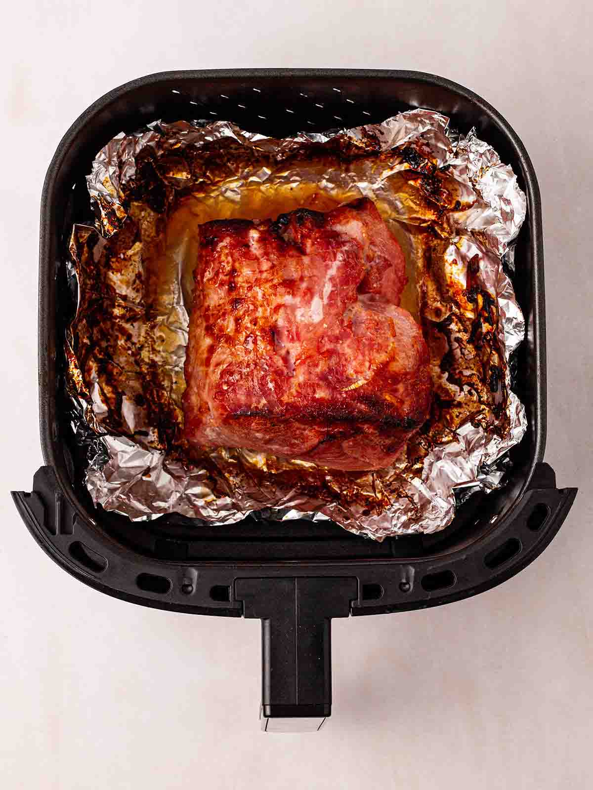 An air fryer tray with a cooked gammon joint sitting on foil inside.