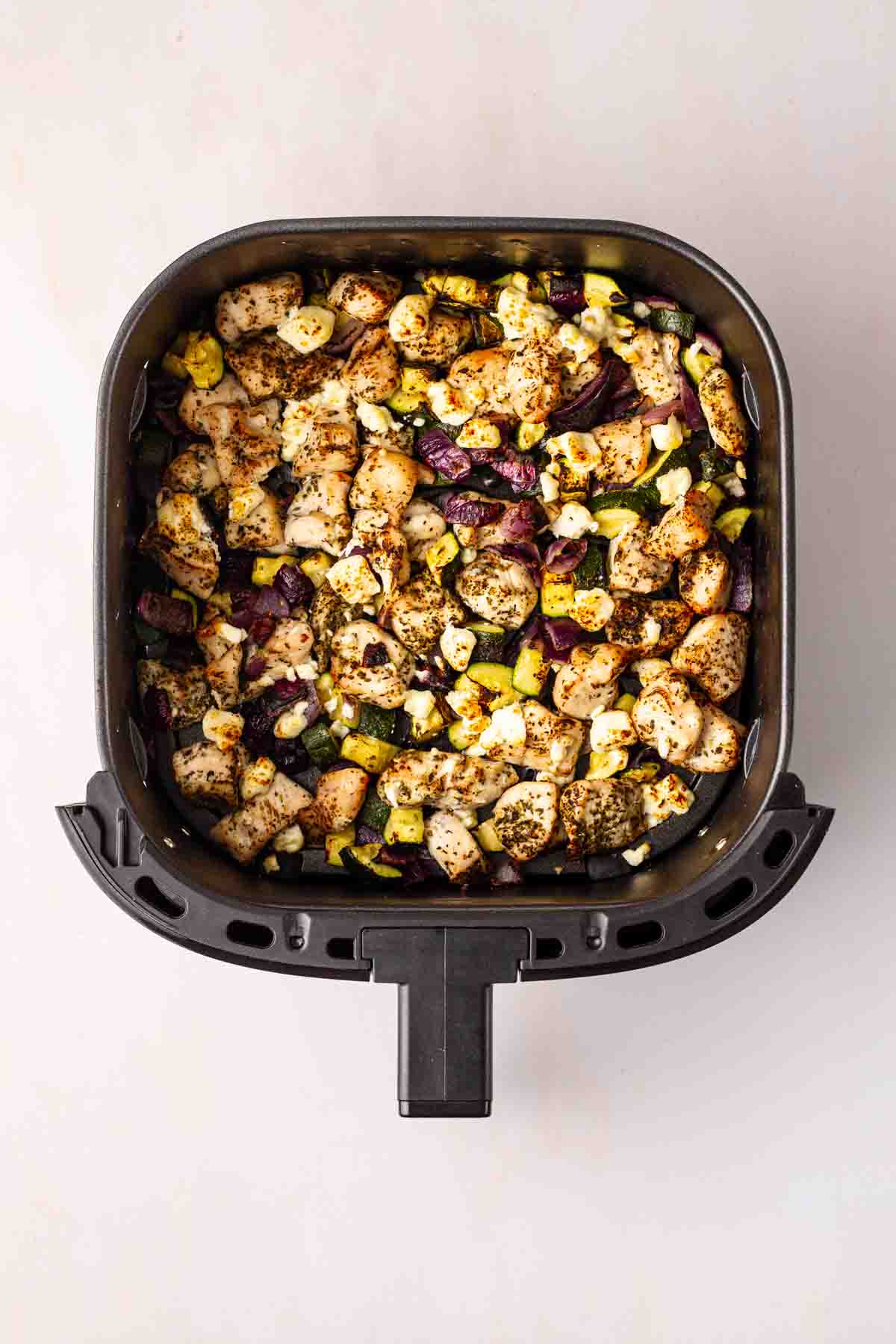 An air fryer with cooked Greek Chicken Traybake and vegetables inside.