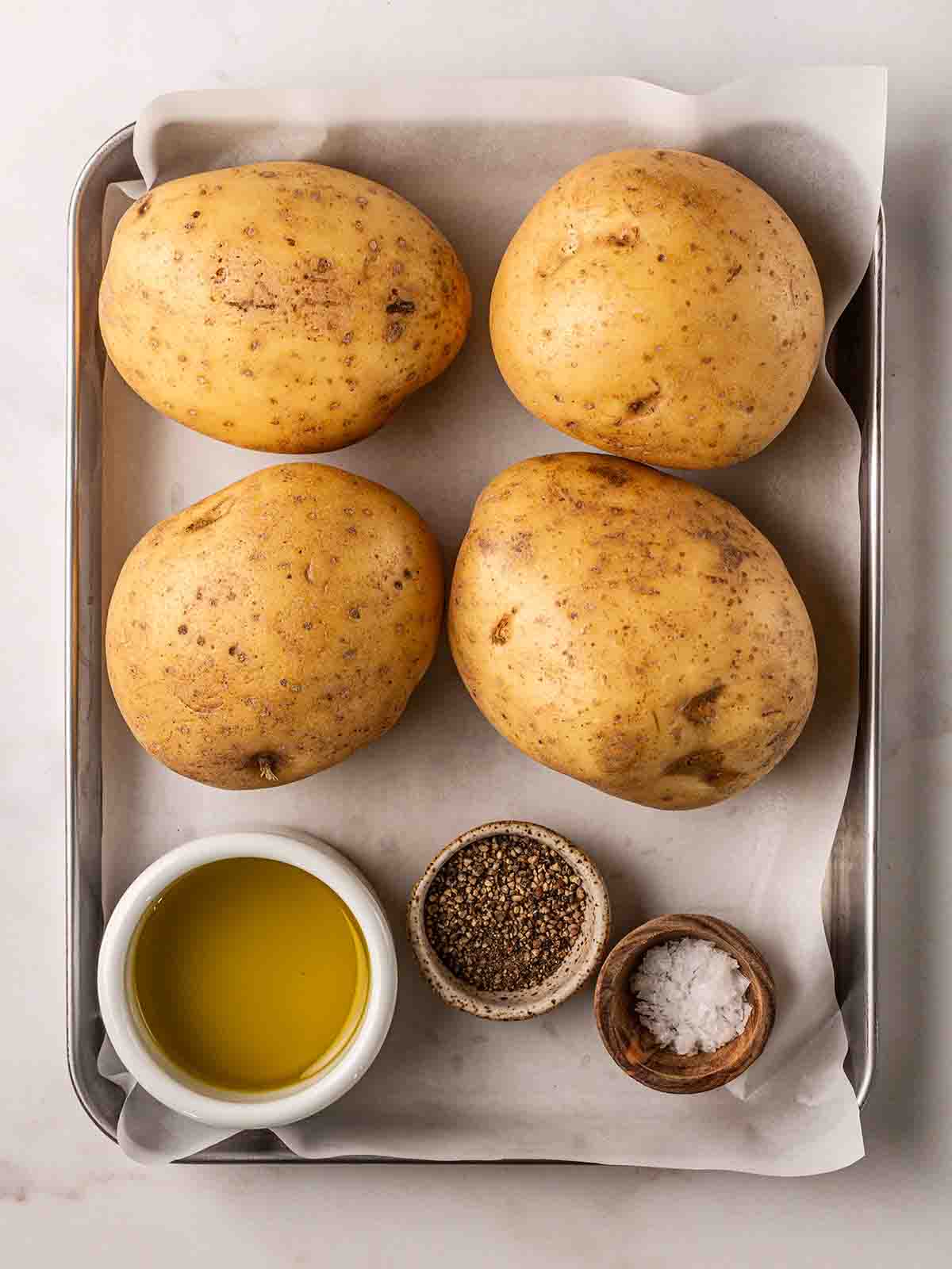 Jacket potatoes, oil and salt and pepper on a baking tray, ready to go in the air fryer.