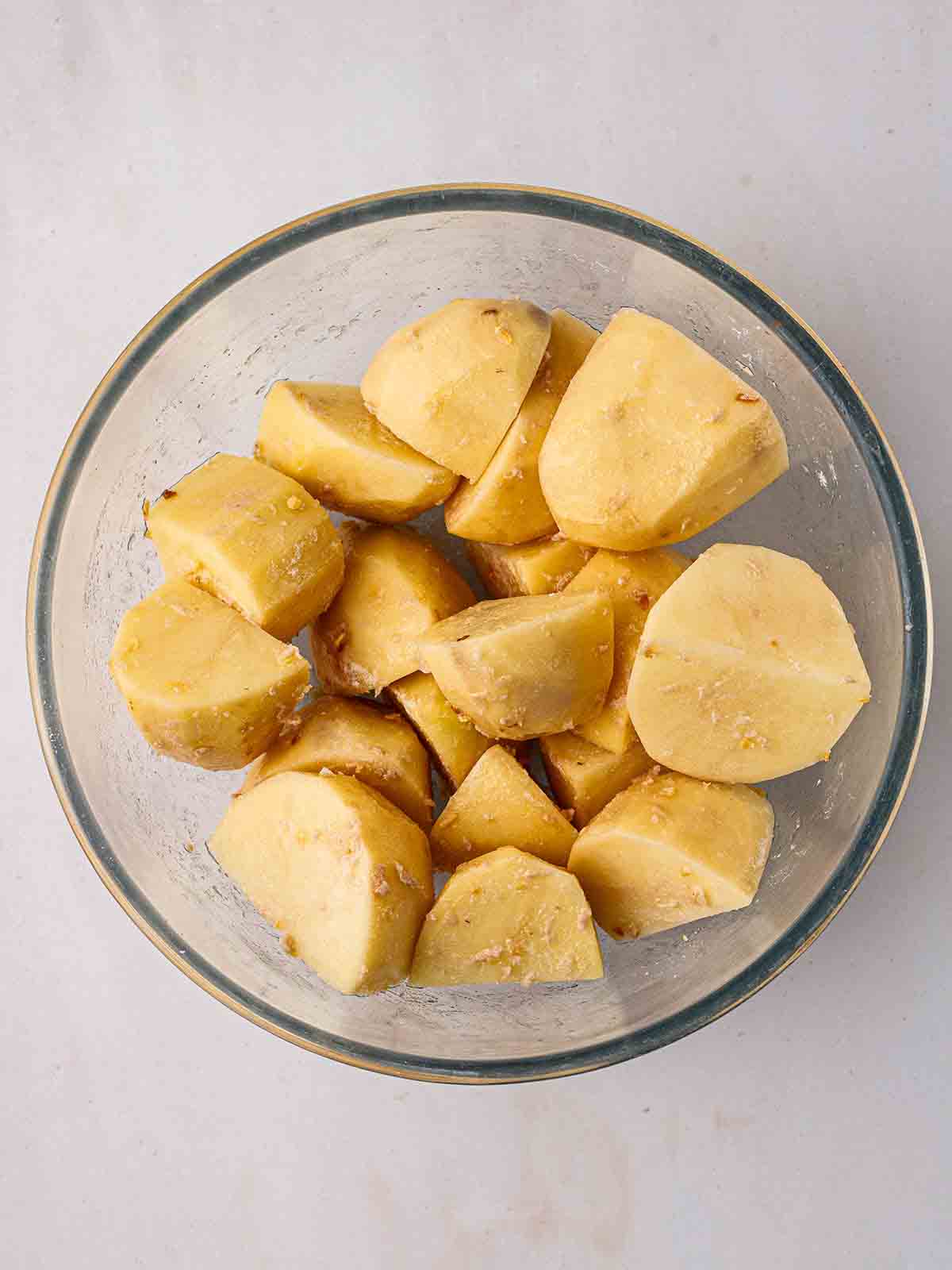 A bowl of peeled, chopped potatoes with onion granules sprinkled over for for step 2 in the recipe for air fryer roast potatoes.
