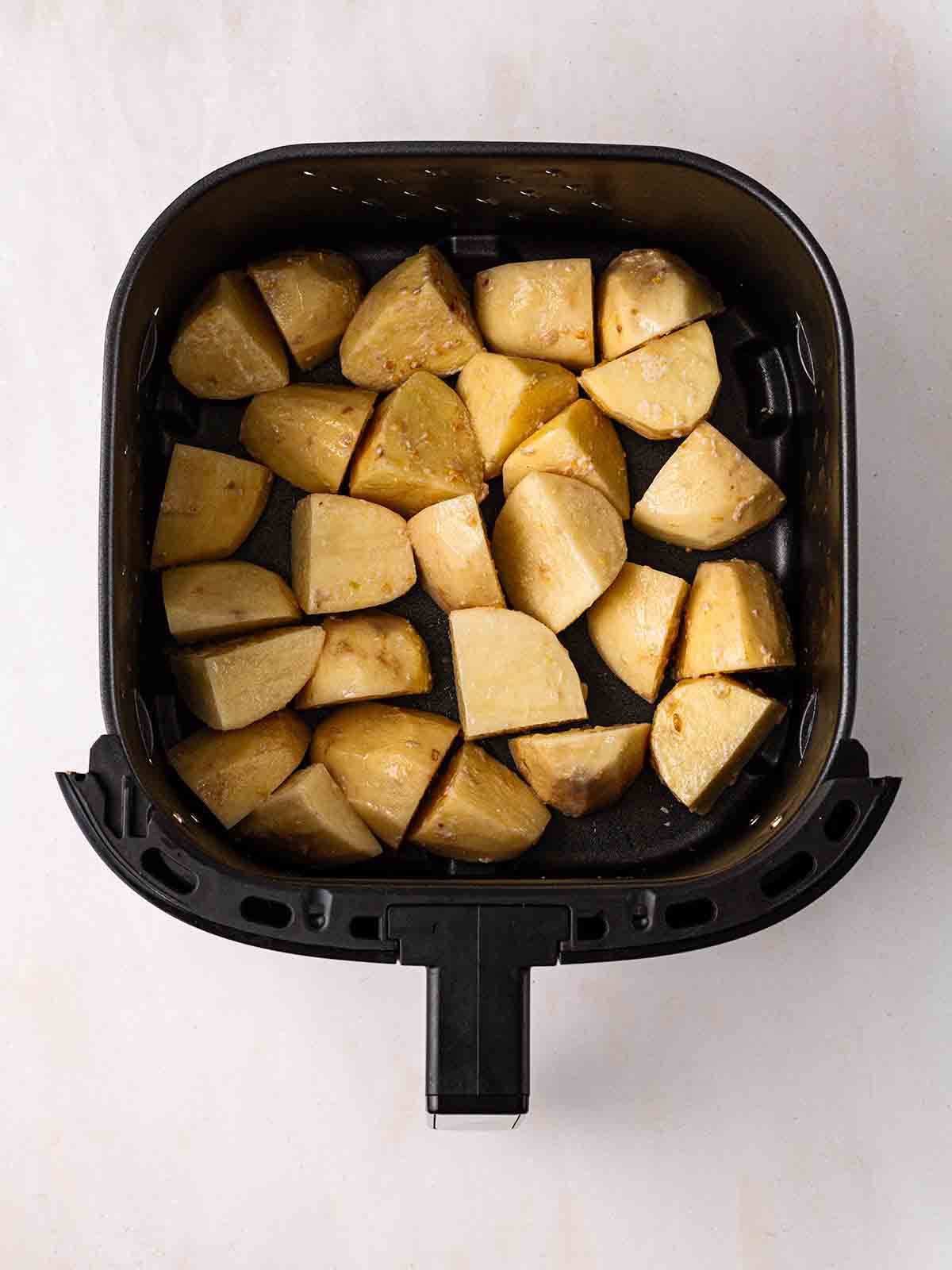 An air fryer filled with uncooked potatoes for step 3 in the recipe for air fryer roast potatoes.
