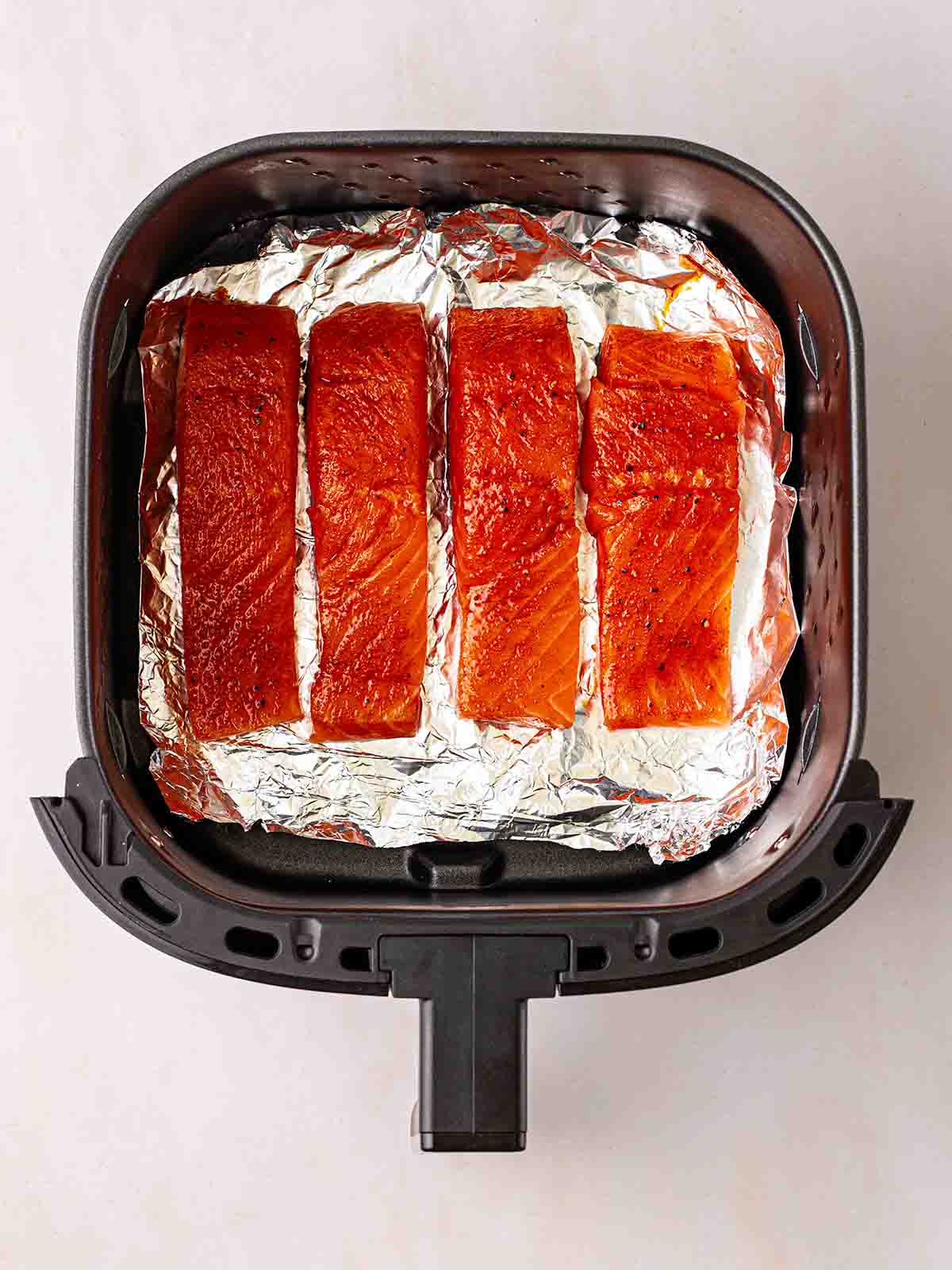 Four fillets of salmon on top of foil in an air fryer tray.