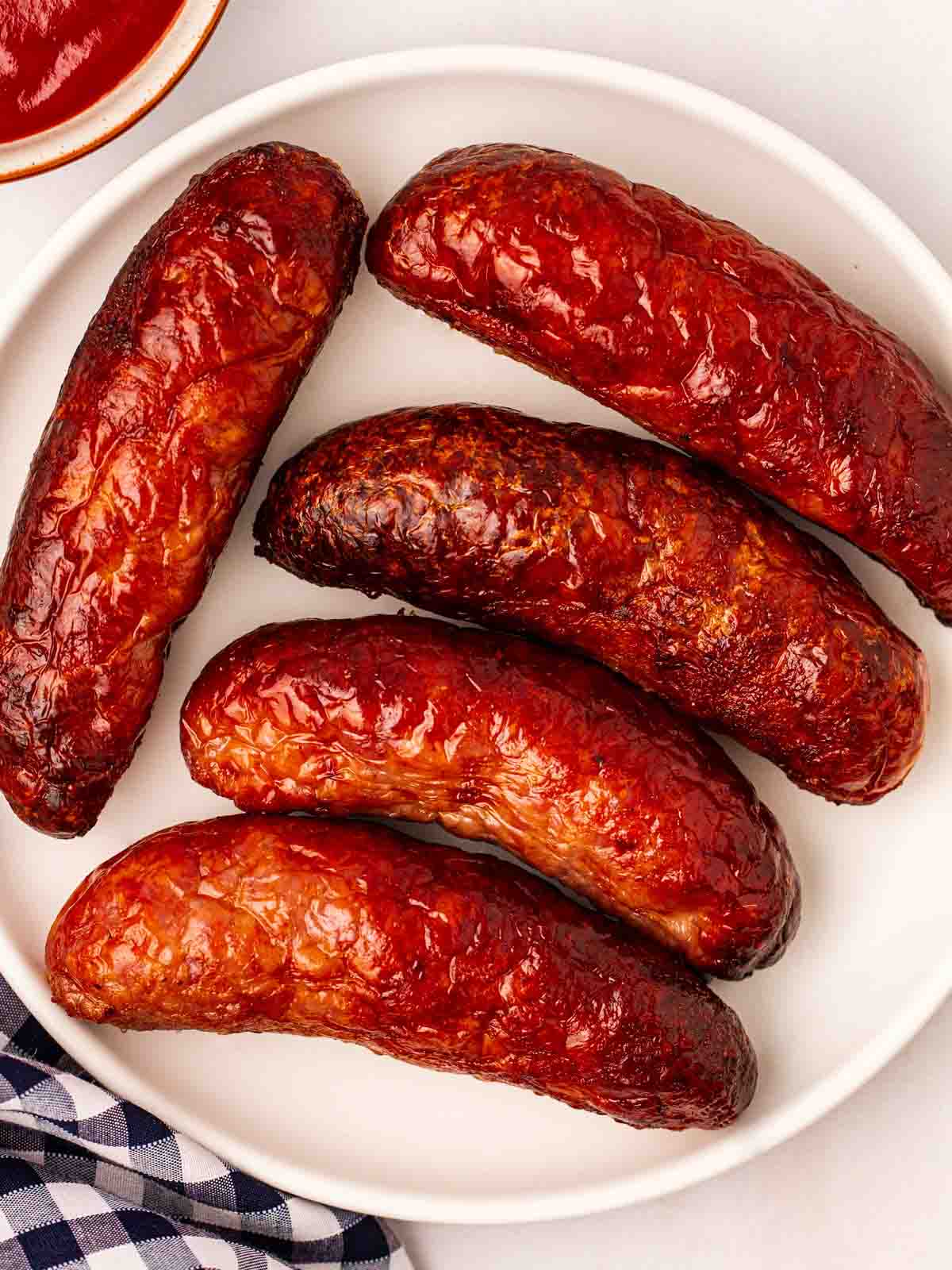 Five fat sausages on a white plate, having been cooked in an air fryer.