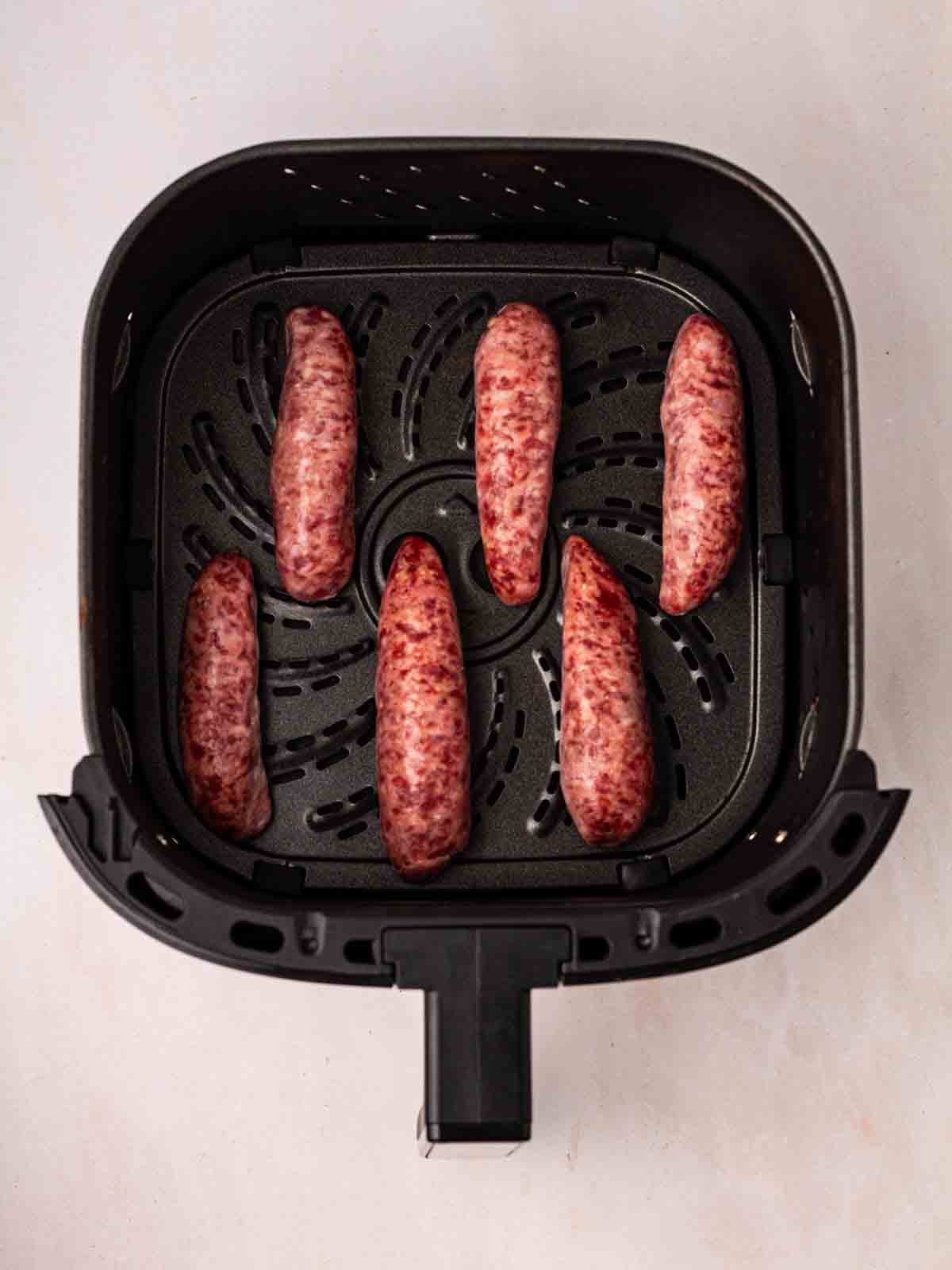 Six sausages in an air fryer pan, with plenty of room between them.