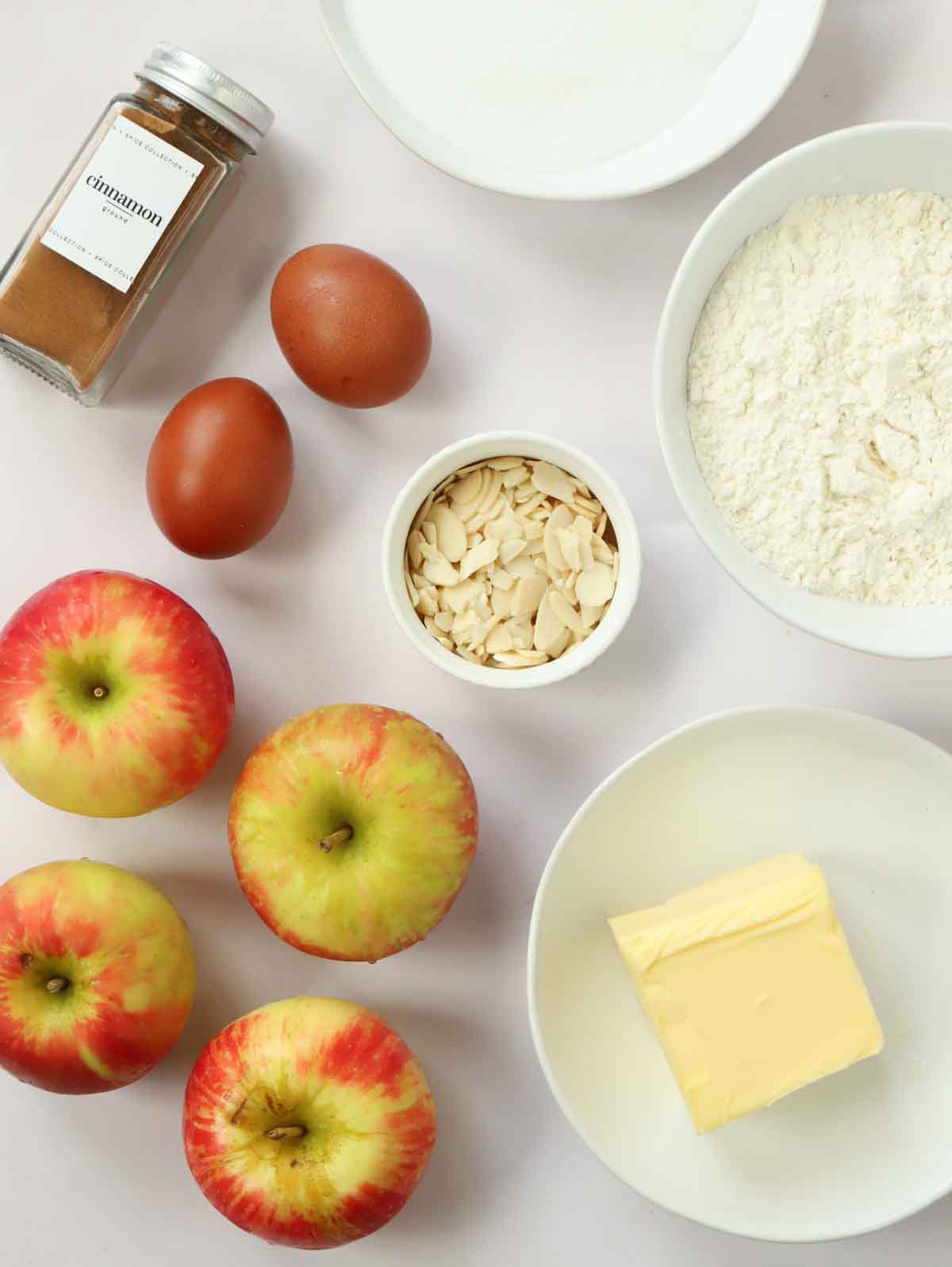 The ingredients for making an Apple Cake laid out on a white counter top.