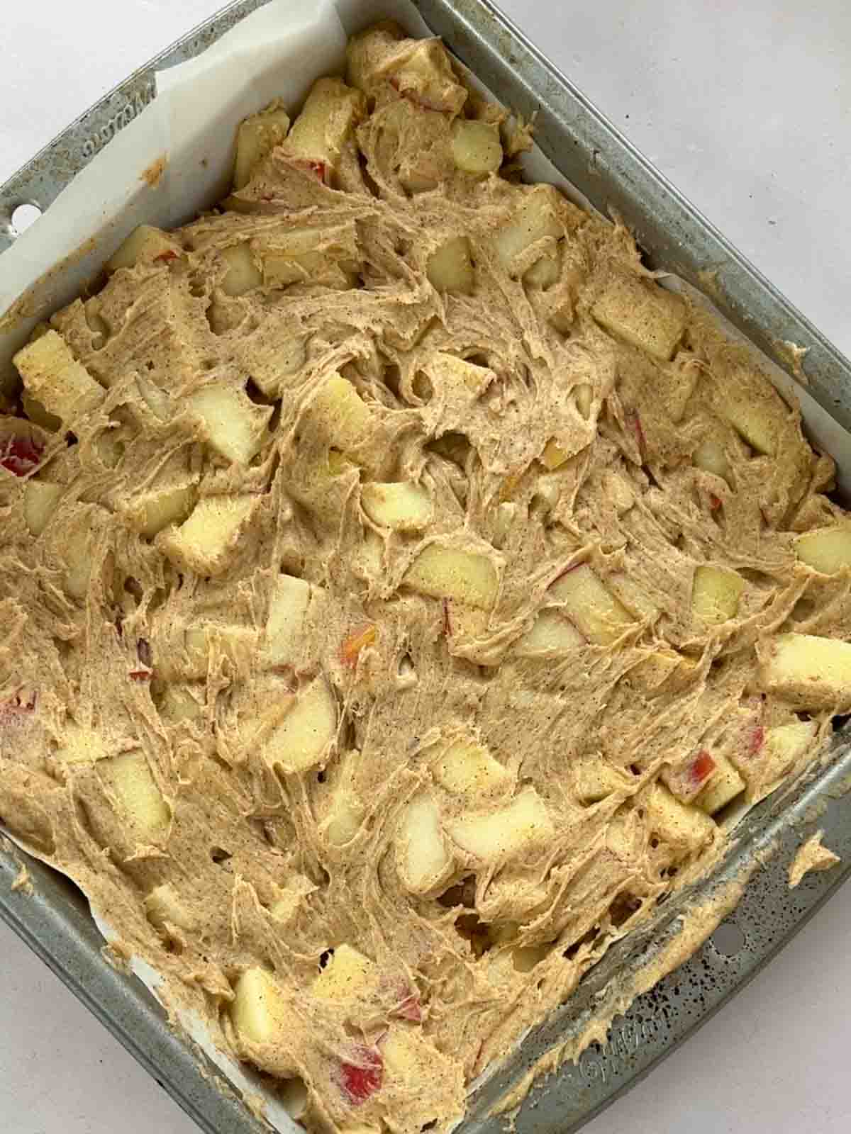 A square oven tin with Apple Cake cake mixture inside, ready to be baked.