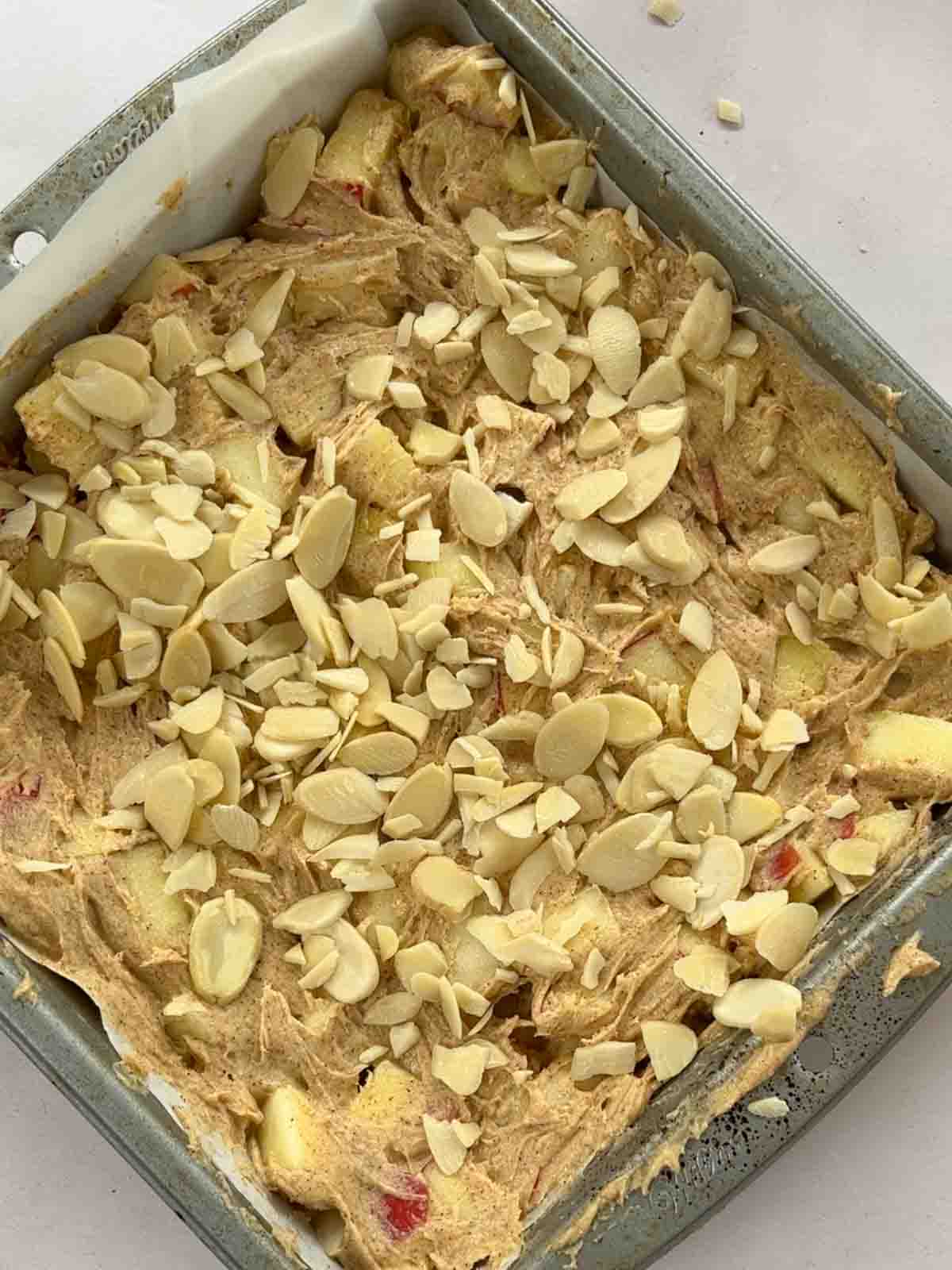 Uncooked apple cake mixture in a baking tin with chopped nuts over the top.