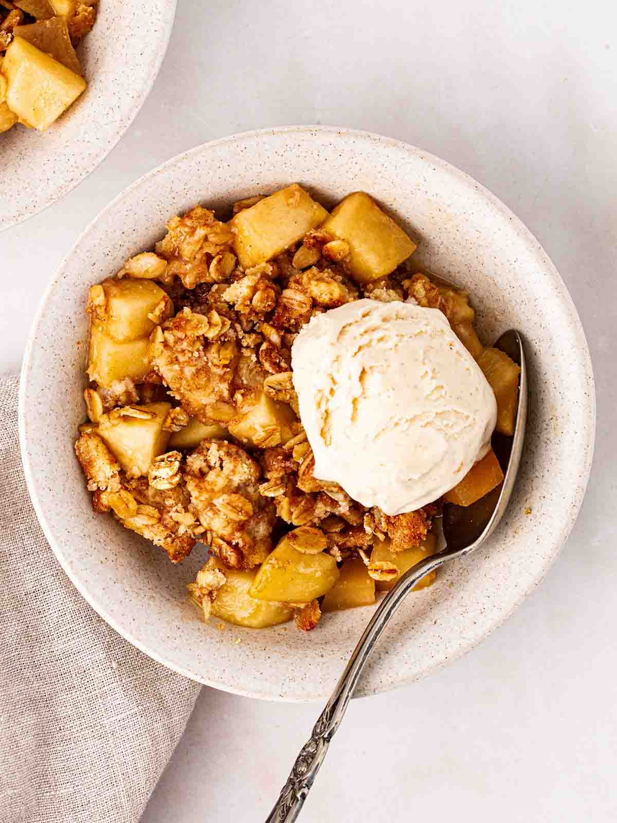 A portion of apple crumble with a spoonful of vanilla ice cream in a white bowl.