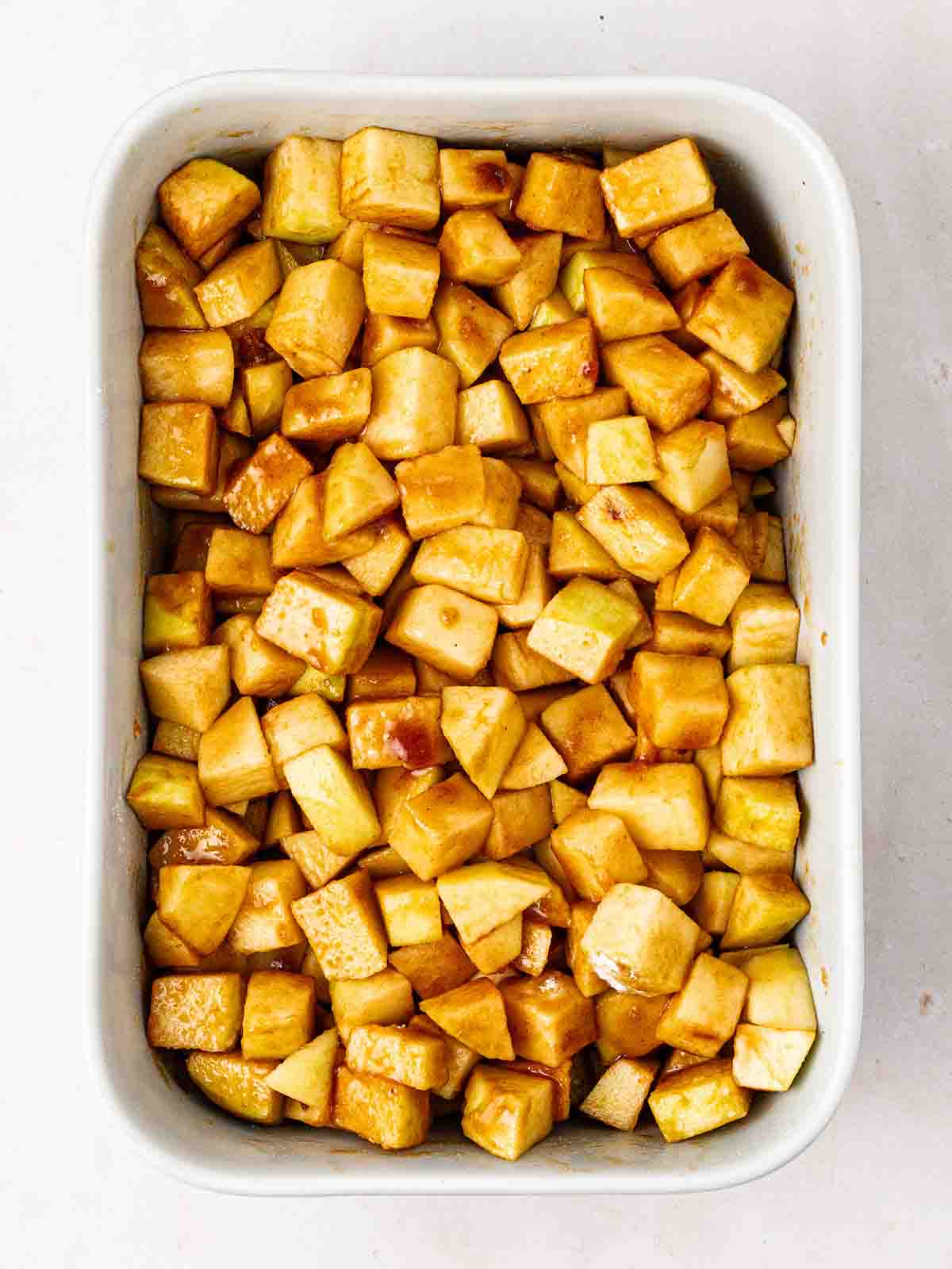 Cubed apple in a baking dish with a sugary filling for step 2 in the recipe for Apple Crumble.