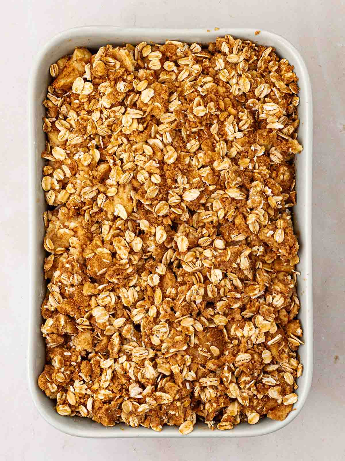An unbaked Apple Crumble from above in a white oven dish, ready to be cooked.