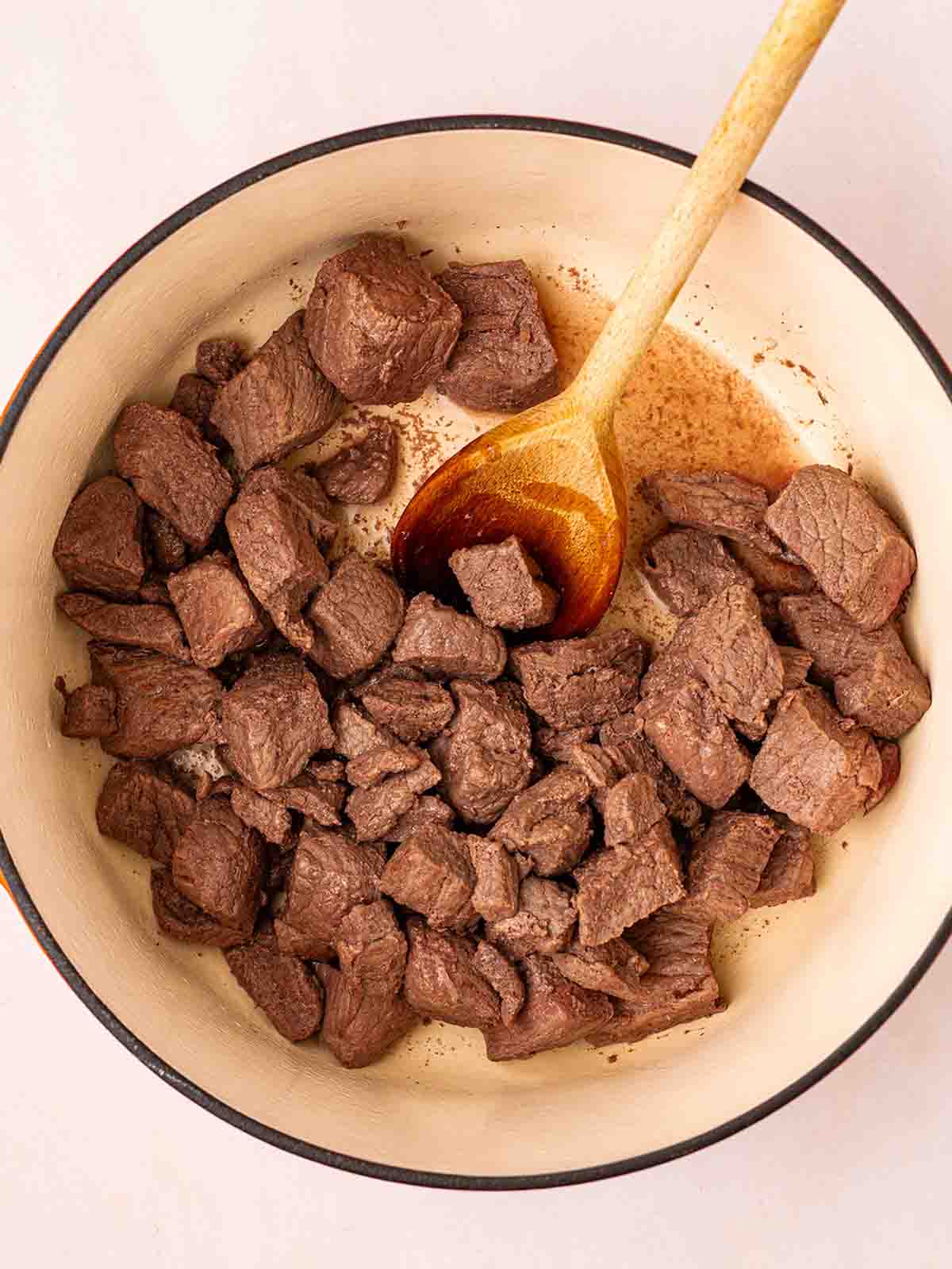 A pan filled with brown chunks of beef in a pan with a wooden soon for step 1 in the recipe for beef bourguignon.