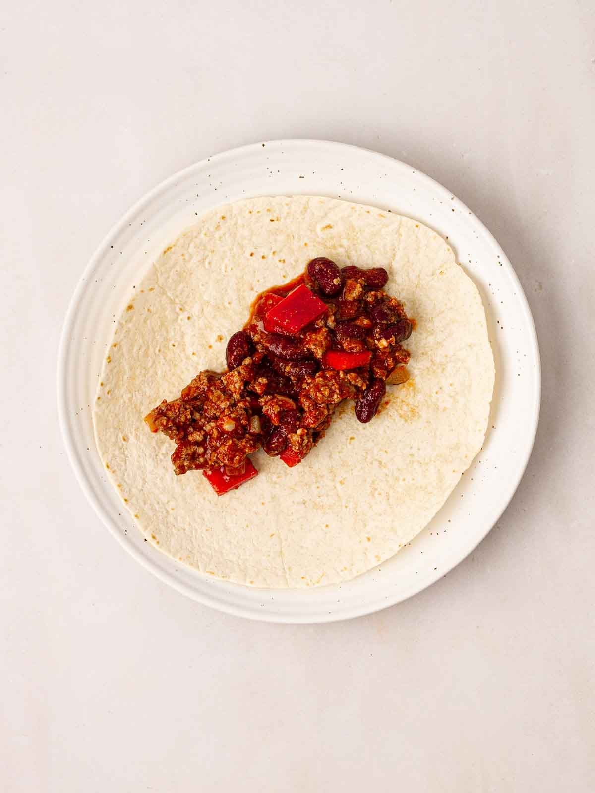 A plate with a tortilla wrap and chilli beef in the middle for step 4 in the recipe for Beef Enchiladas.