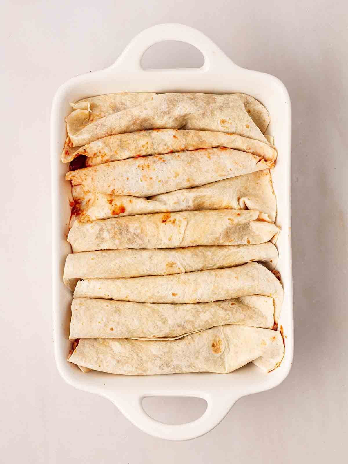 An oven dish with rolled tortilla wraps for step 5 in the recipe for Beef Enchiladas.