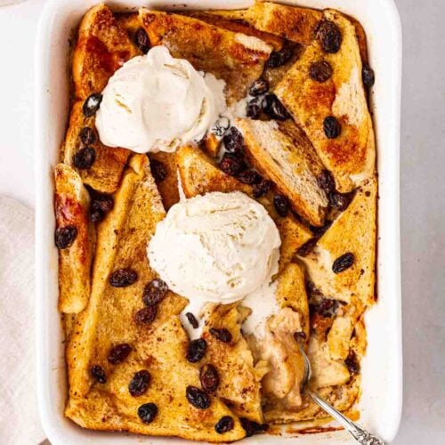 A white oven dish with cooked bread and butter pudding, topped with vanilla ice cream.