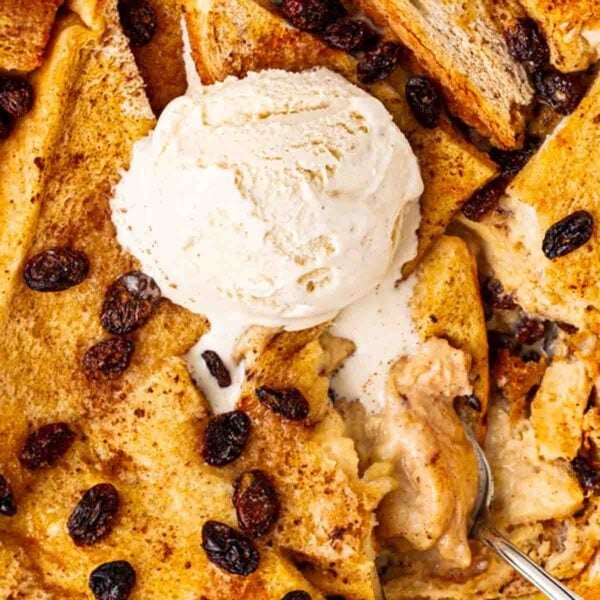 A close up of bread and butter pudding with raisins and a dollop of ice cream.