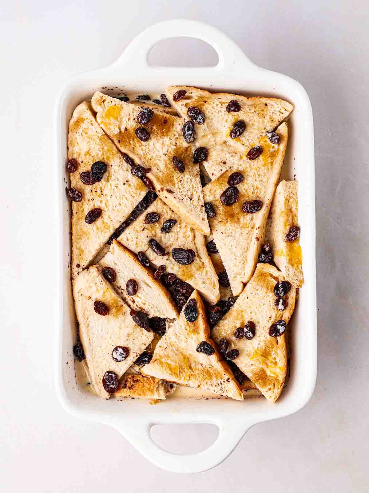 A white dish filled with traditional bread and butter pudding with raisins.
