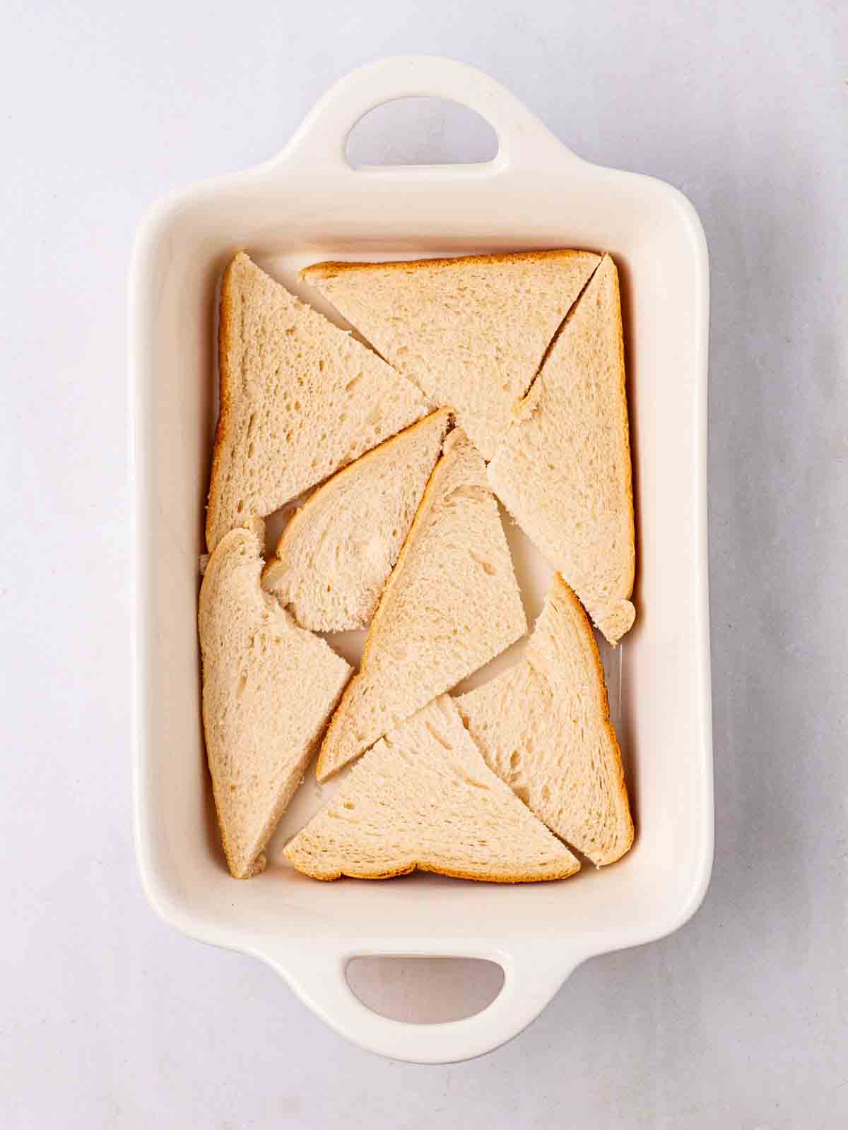 Triangles of white bread in a white oven dish for step 1 in the recipe for Bread and Butter Pudding.