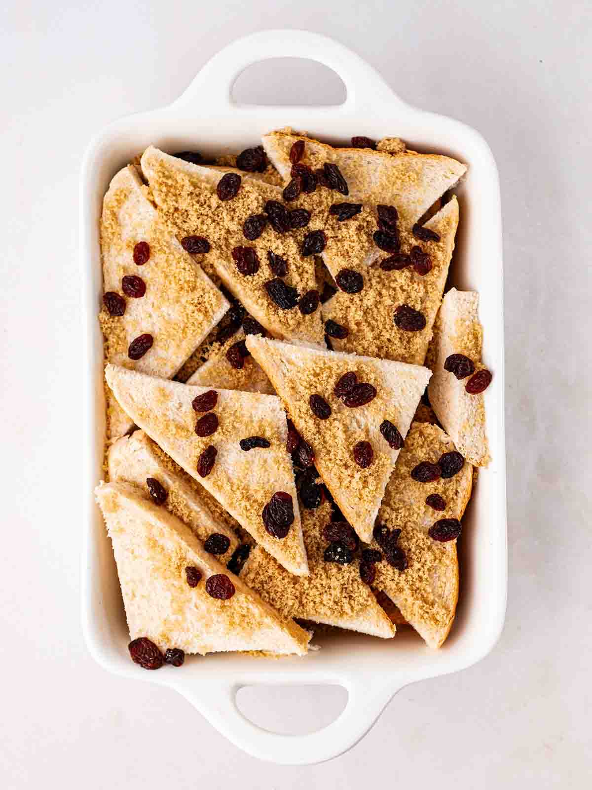 Triangles of white bread with raisins and sugar on top for step 3 in the recipe for Bread and Butter Pudding.
