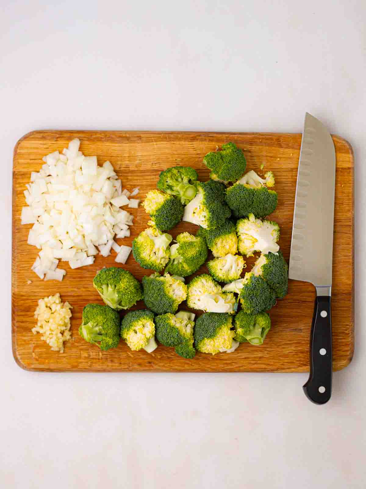 A chopping board with a knife, chopped up broccoli and onion ready to make Broccoli and Stilton Soup.
