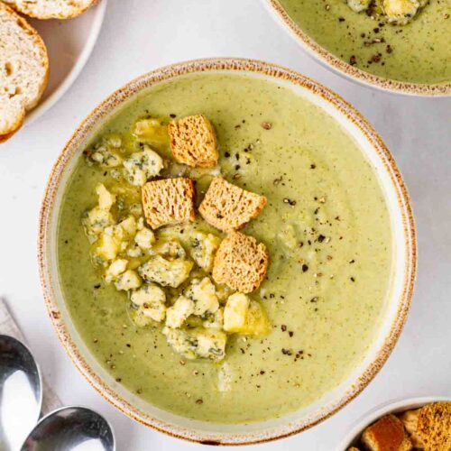 A white table with Broccoli and Stilton Soup bowls on top, ready to eat.