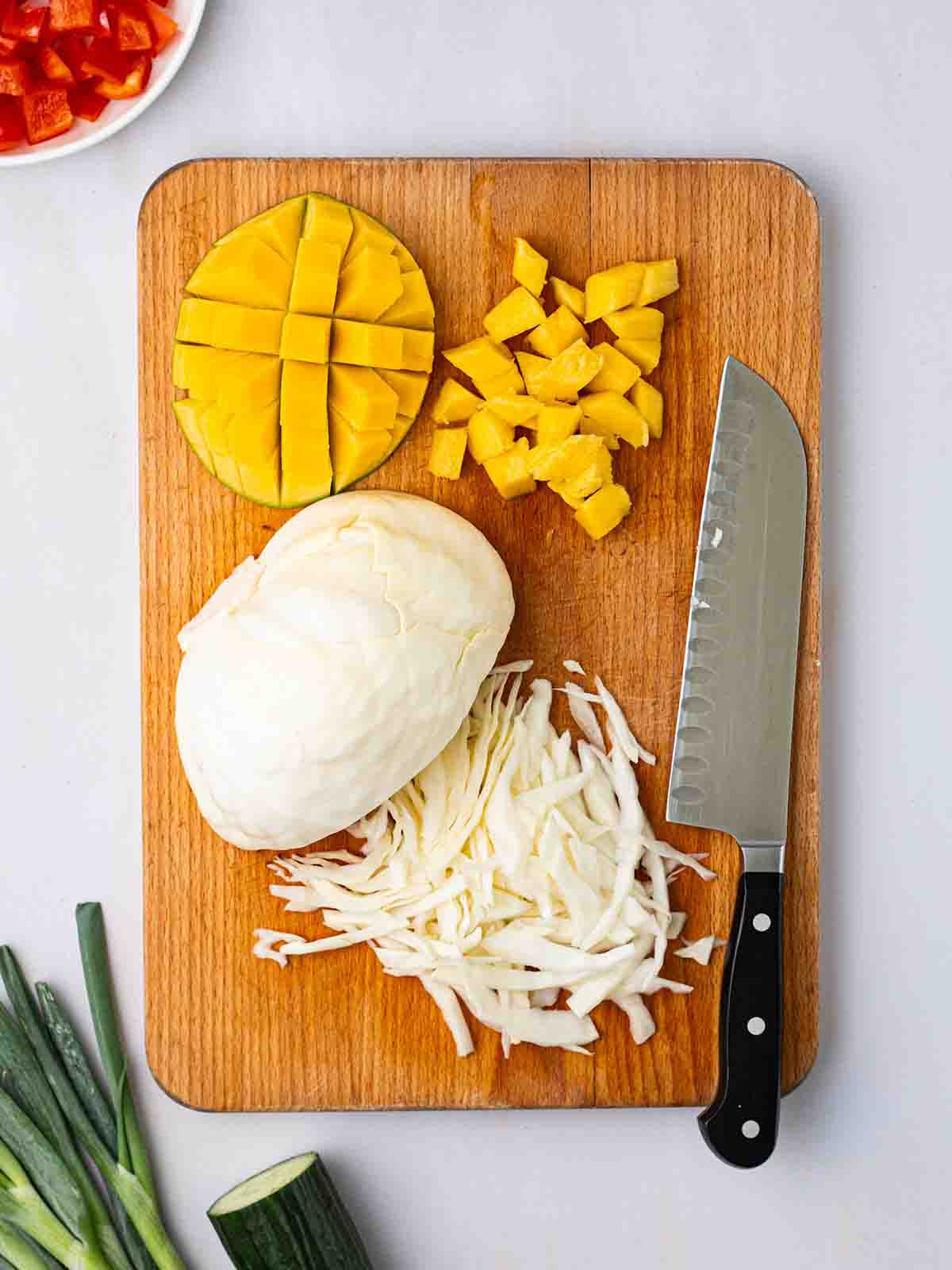 A chopping board with sliced cabbage and mango with other ingredients around for a Cabbage Salad in progress.