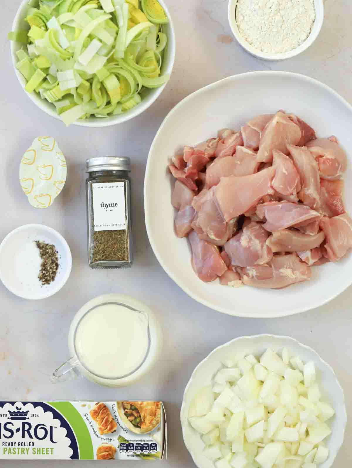 The ingredients for making a Chicken and Leek Pie with Puff Pastry laid out on a white counter top in bowls.