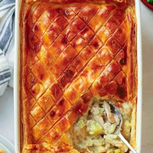 A pie dish filled with cooked Chicken and Leek Pie, being served with a spoon.