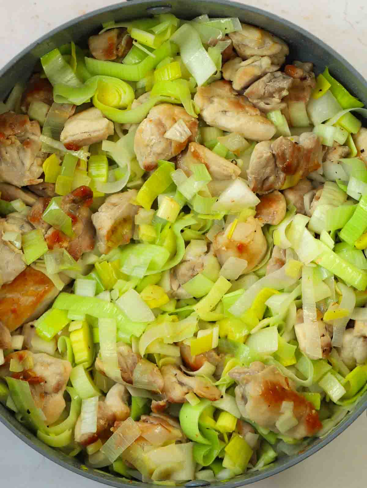 Browned chicken pieces and leek in pan cooking for step 2 in the recipe for Chicken and Leek Pie.
