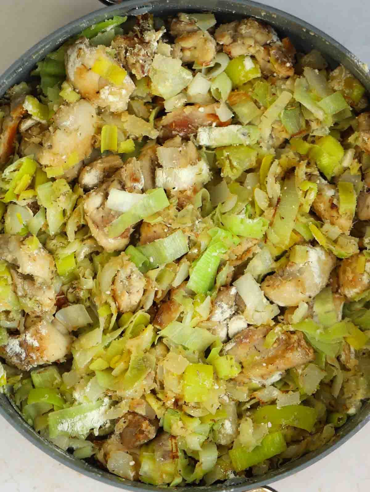 Chicken and leeks in a pan with flour sprinkled over for for step 3 in the recipe for Chicken and Leek Pie.
