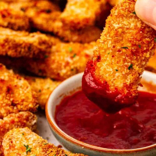 A chicken goujon being dipped into ketchup.