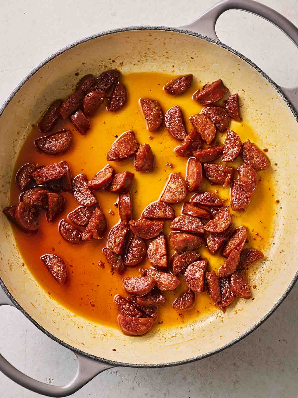 Chunks of chorizo frying in a pan for step one in the recipe for how to make Chorizo Orzo.