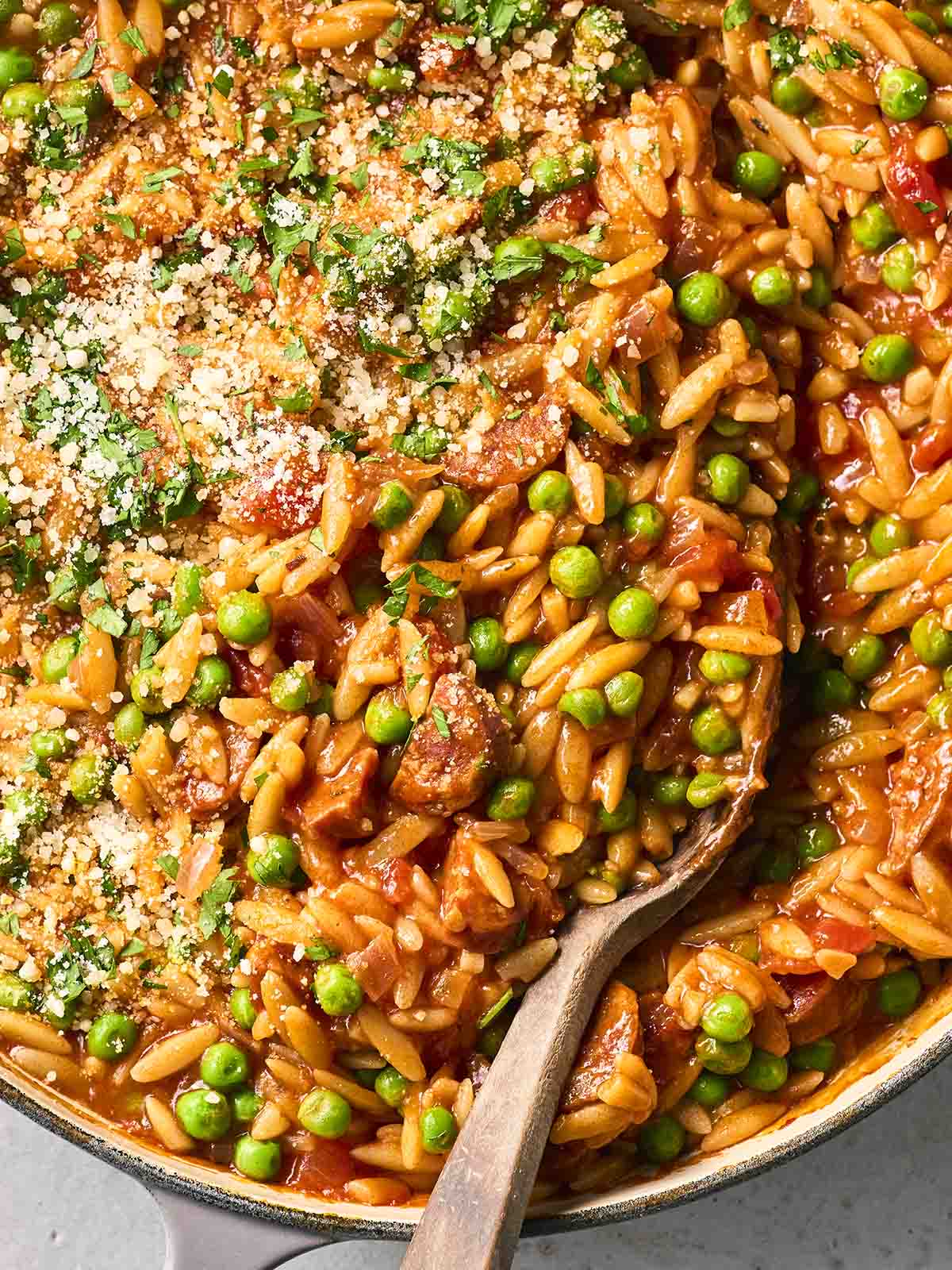 Pan of chorizo orzo with peas and wooden spoon in.