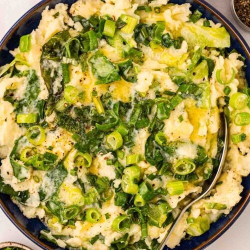 A blue bowl with Colcannon inside, with a spoon to serve and pinch pots of salt and pepper to the side.