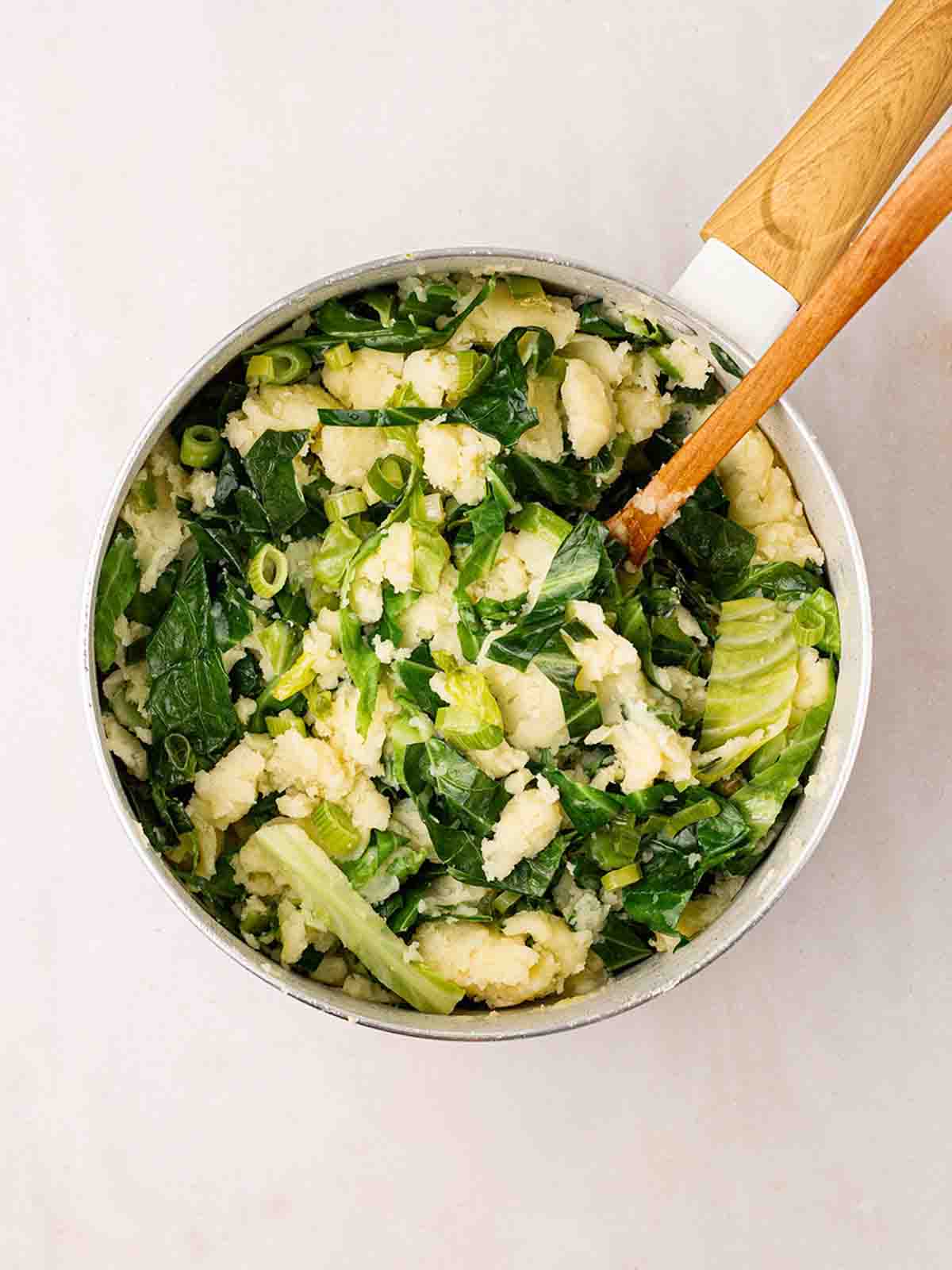 Mashed potato with cabbage in a pan with a wooden spoon for step 4 in the method for Colcannon recipe.