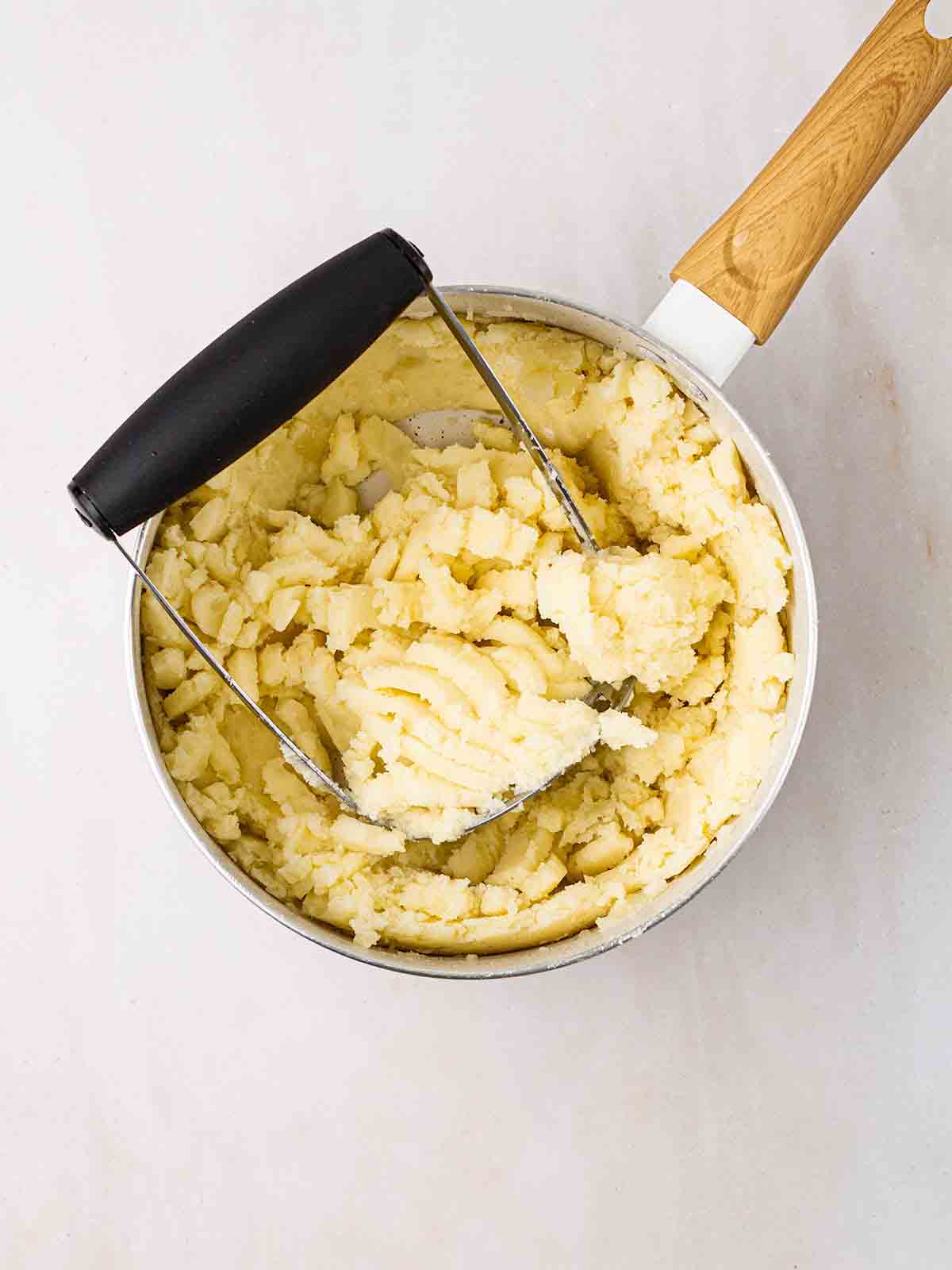 Potato being mashed for step 3 in the recipe for colcannon.