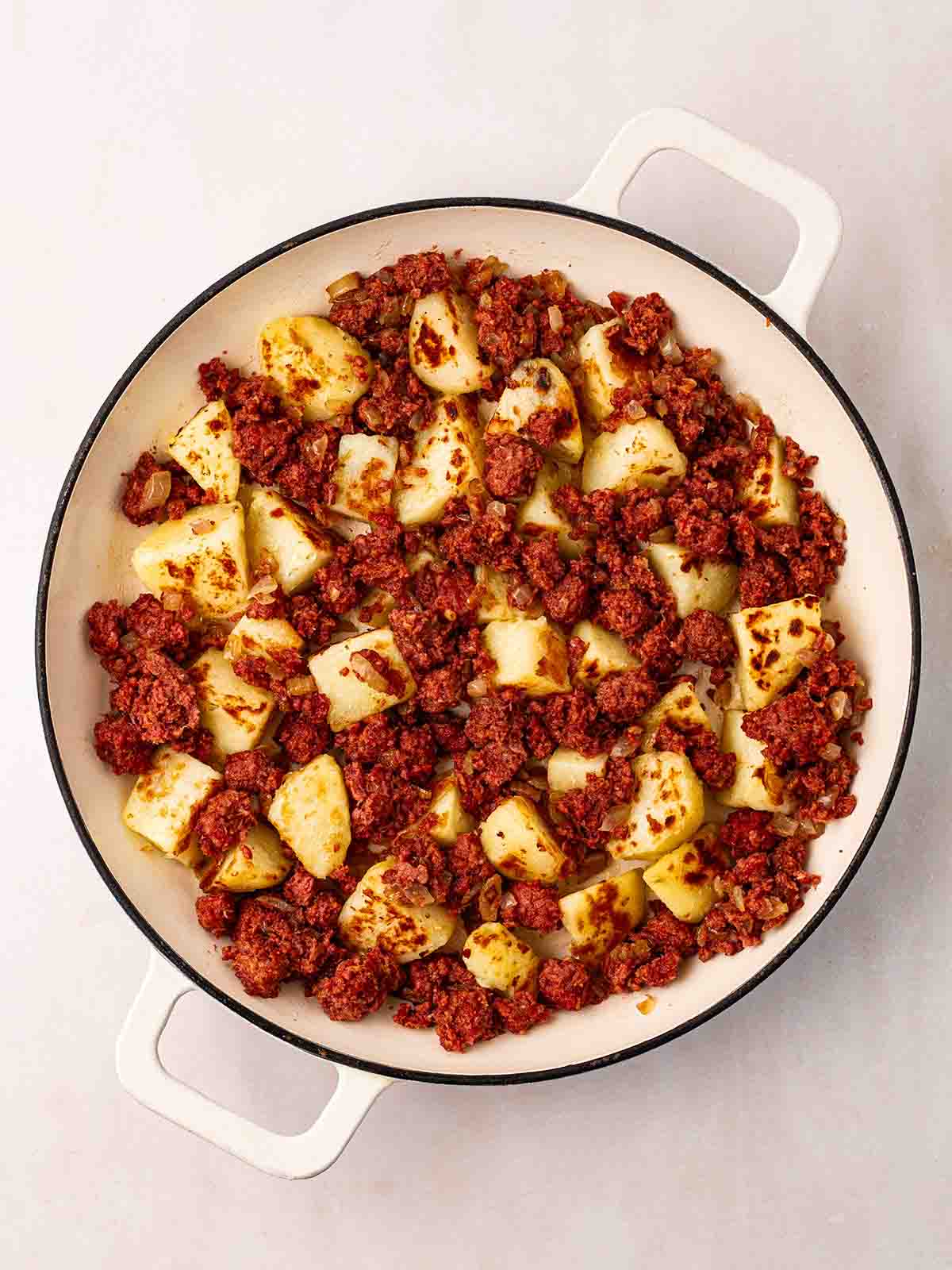 A pan filled with cubed potatoes and tinned corned beef for step 2 in the recipe for traditional Corned Beef Hash.