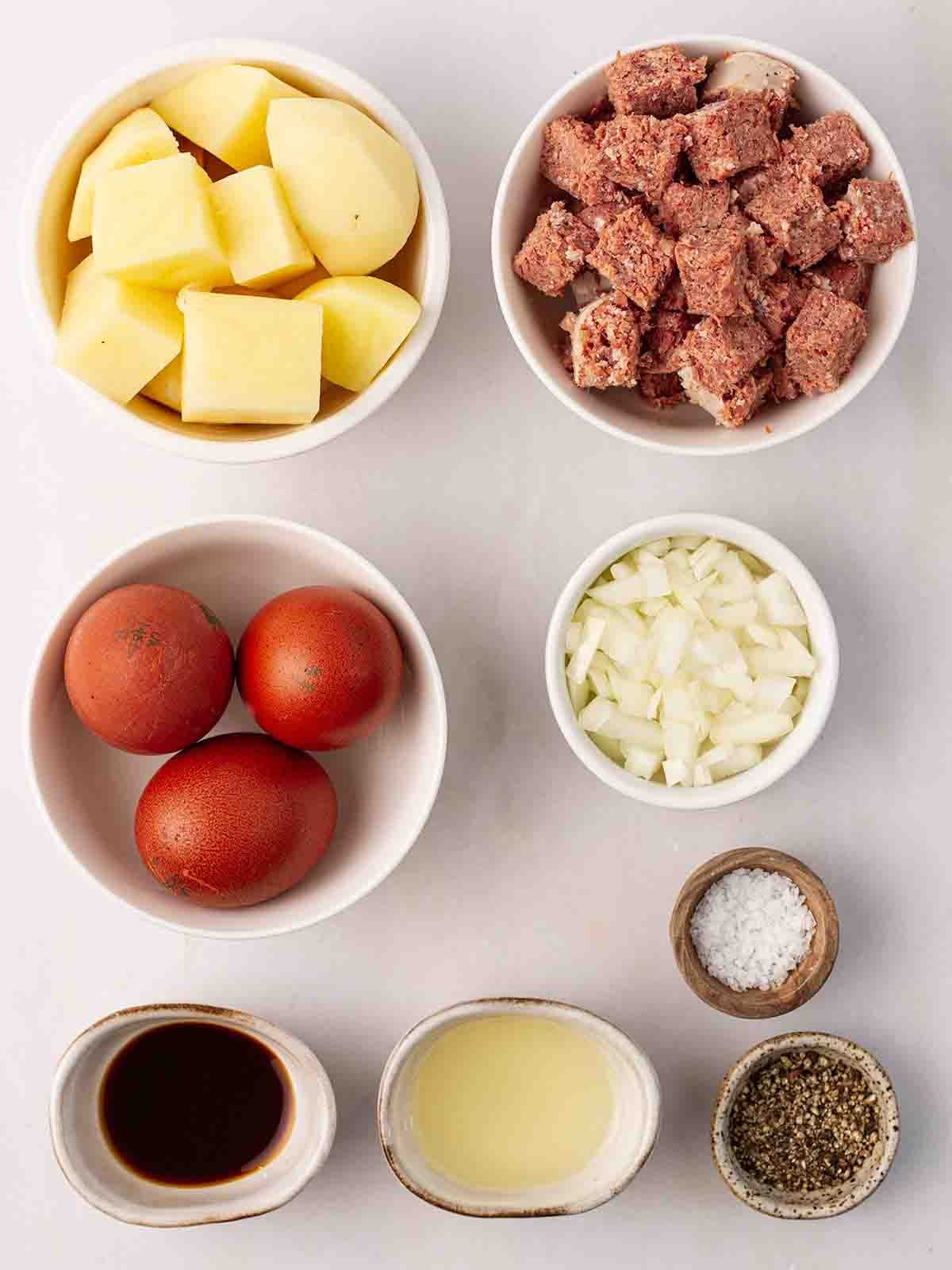 The ingredients for making Corned Beef Hash laid out in small bowls on a white surface.