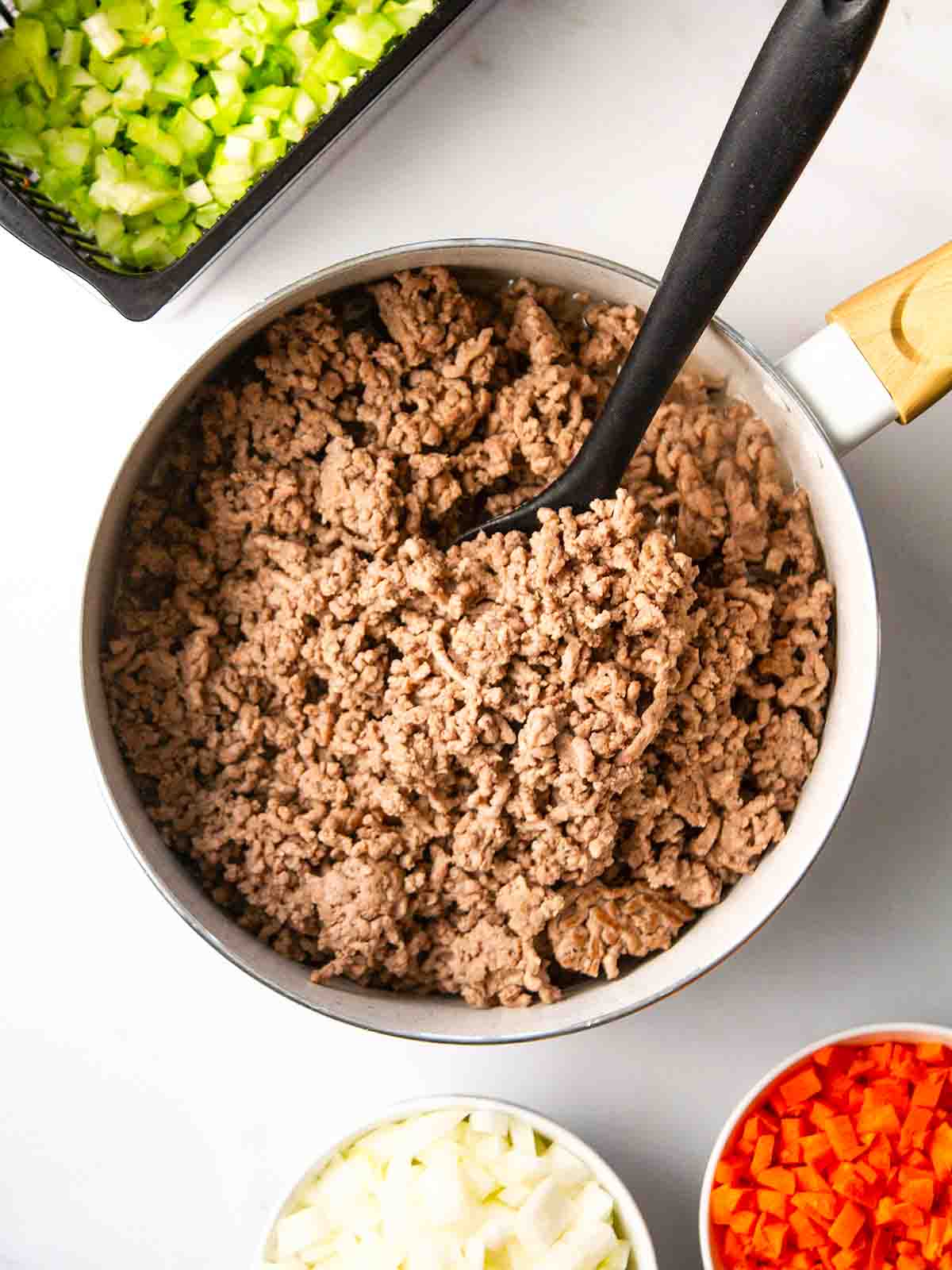 A pan filled with browned mince beef with veggies to the side for step 1 in the recipe for Cottage Pie.