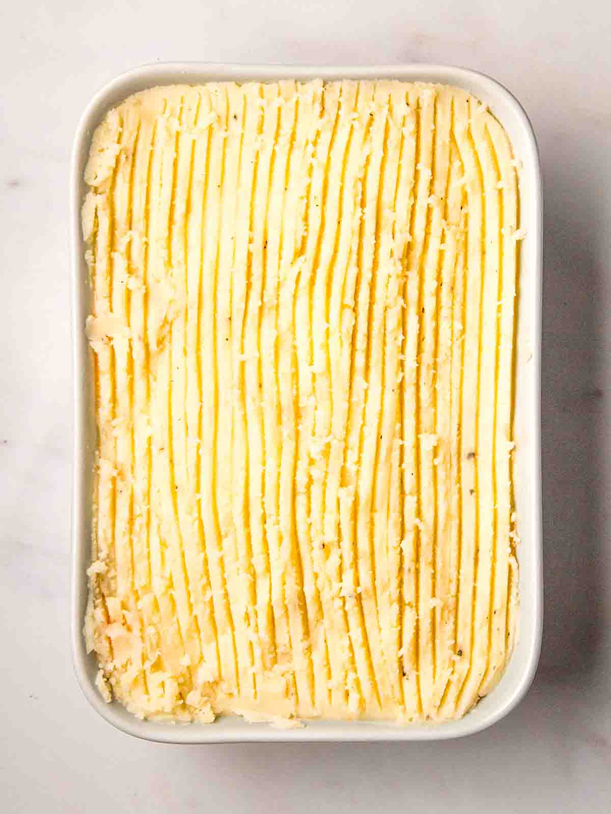 An uncooked Cottage Pie in a dish, ready to bake.