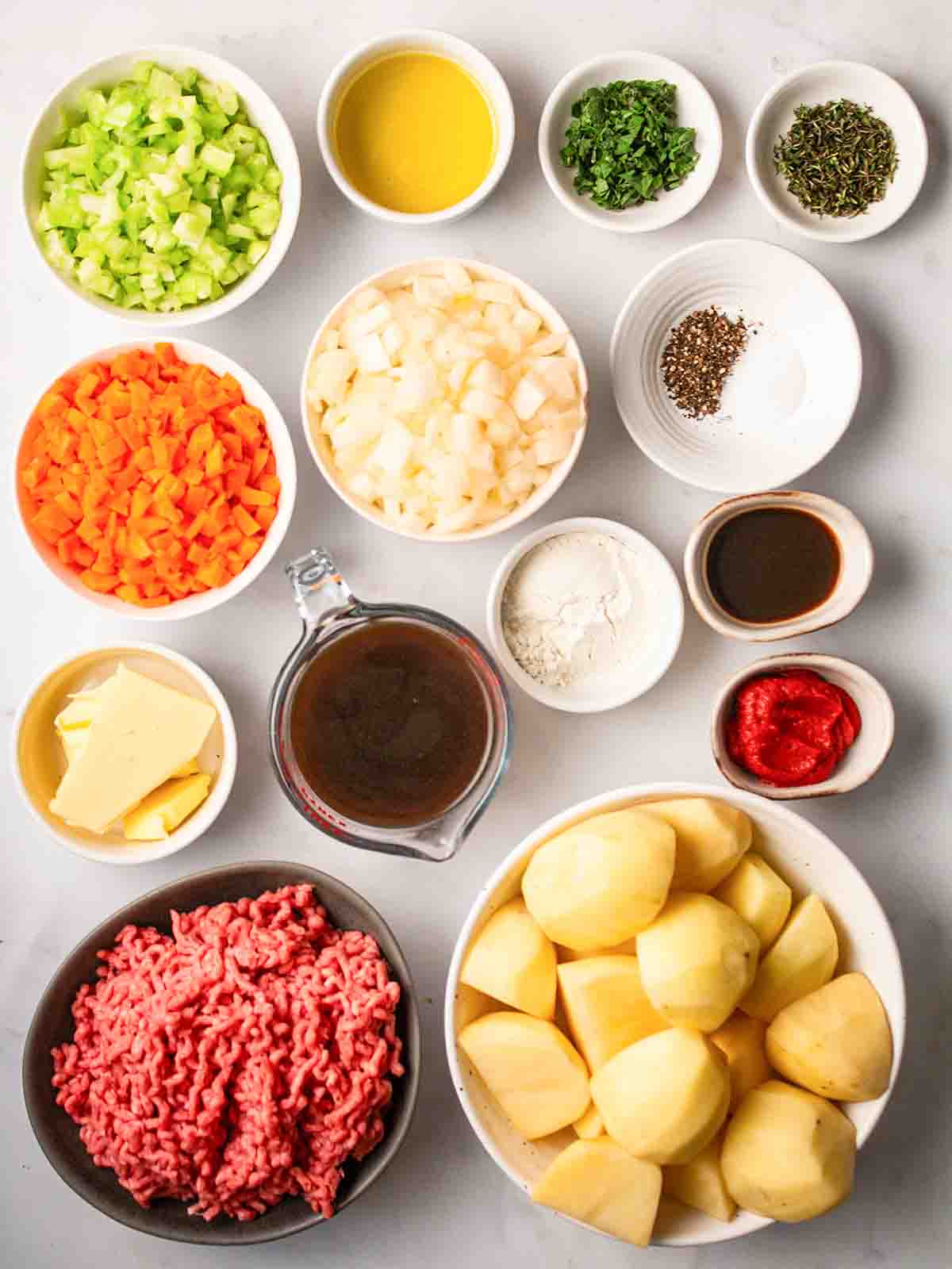 The ingredients for making a Cottage Pie recipe laid out in small bowls on a white counter.