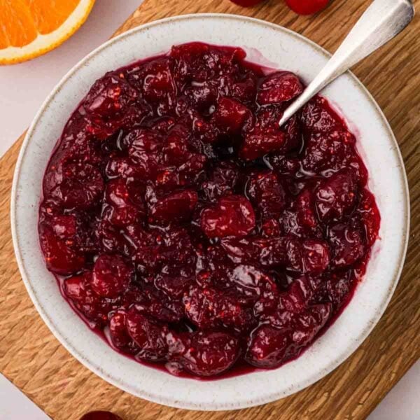A white bowl filled with homemade cranberry sauce, with a spoon sticking out.