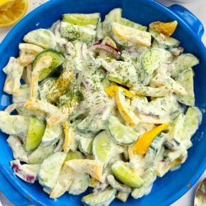 A blue salad bowl filled with cucumber salad with yoghurt dressing.