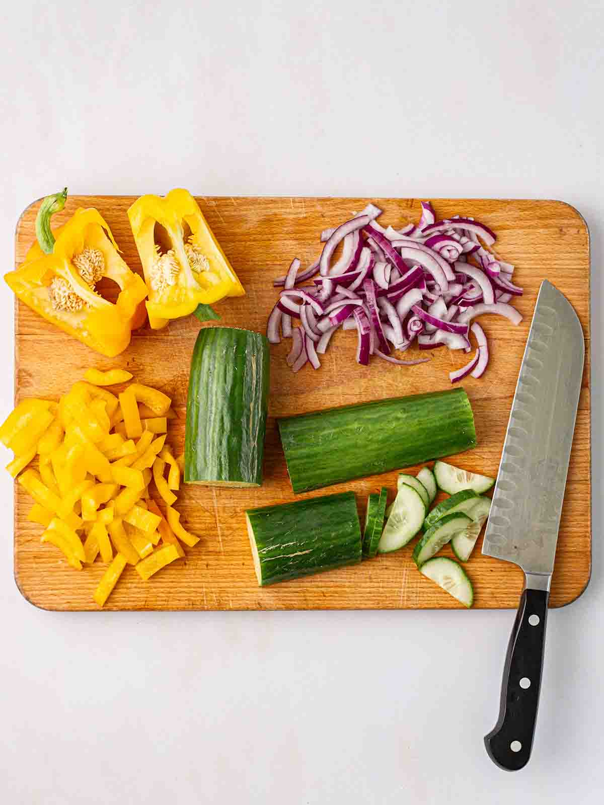 A chopping board with chopped salad and a large knife for step 1 in the recipe for Cucumber Salad.