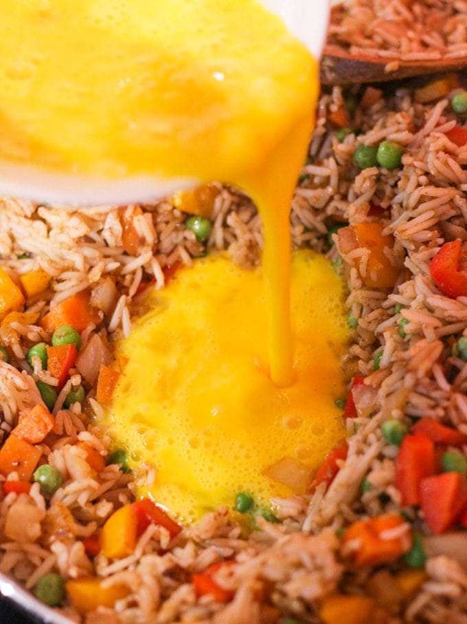 Fried rice in a pan with egg being poured in for egg fried rice. How to make Egg Fried Rice, step 4.