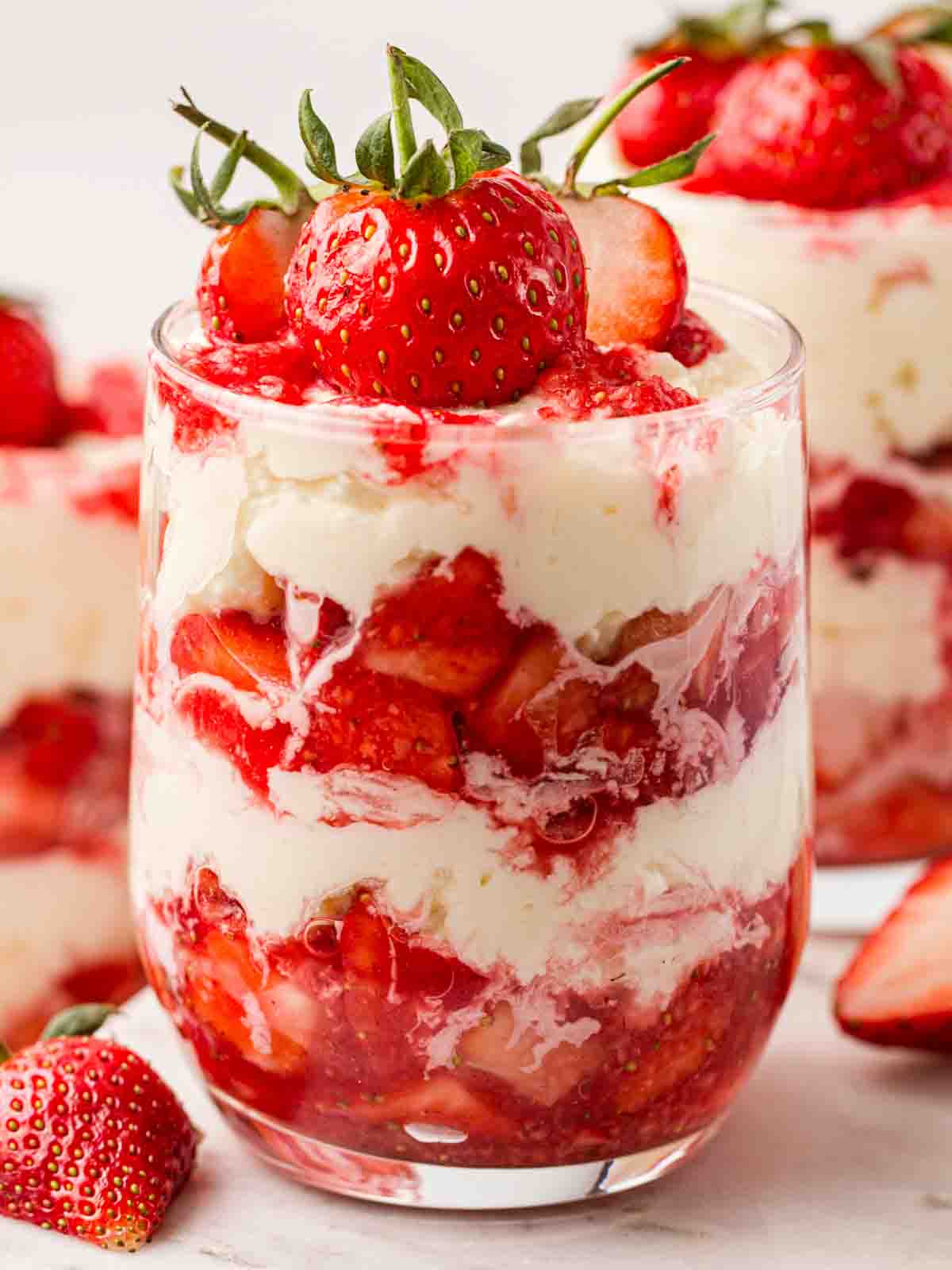A glass filled with Eton Mess, layers of strawberries and cream and meringue, topped with strawberries.